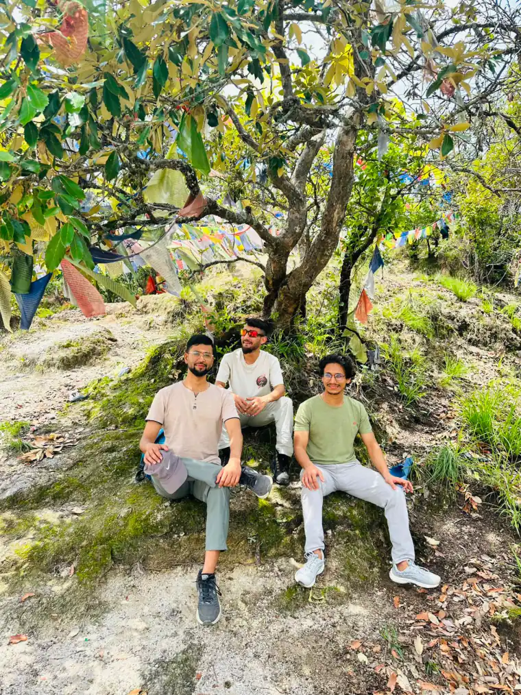 Three NepalHRM teammates taking a break under a prayer-flag-draped tree during a team hike above the Kathmandu Valley