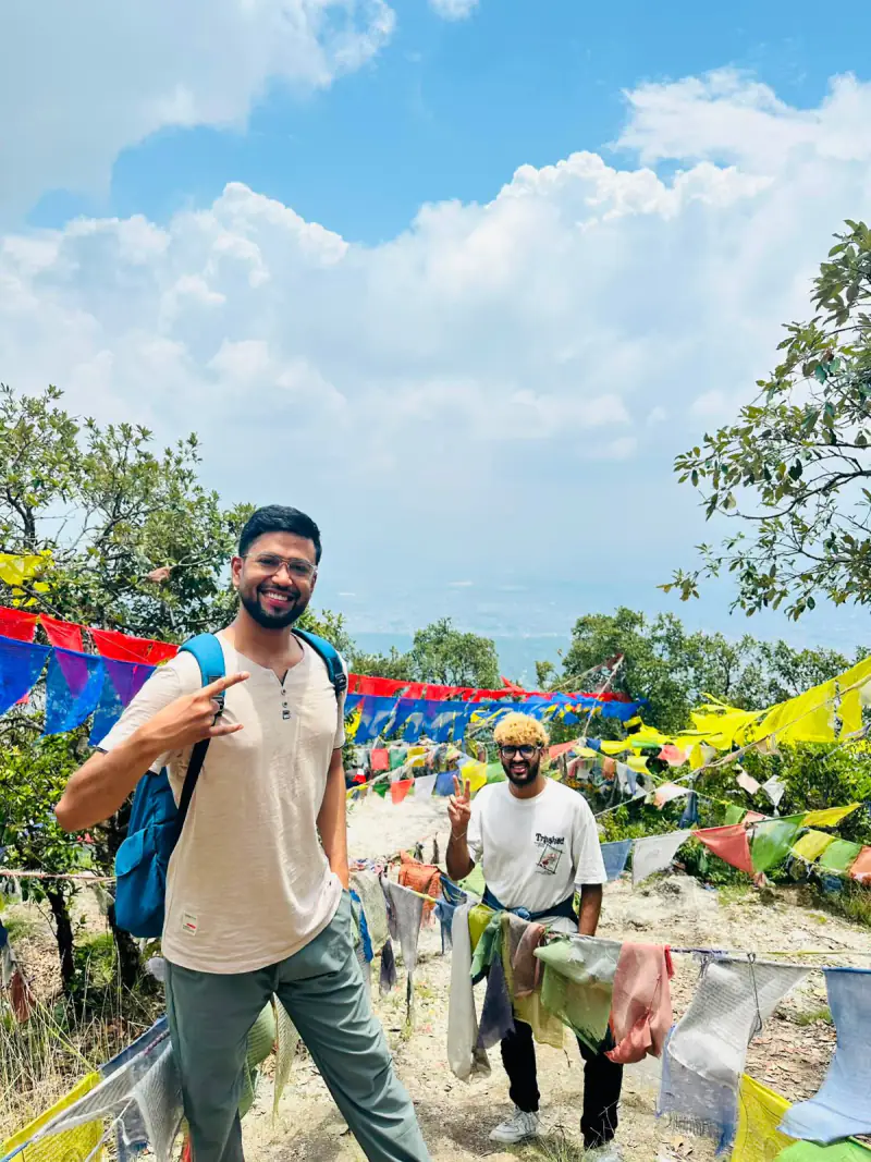 Two NepalHRM teammates at a hilltop viewpoint framed by colourful Buddhist prayer flags on a team day out near Kathmandu